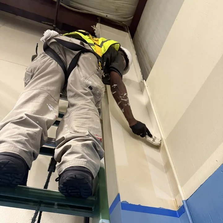 Painter in coveralls rolling a commercial interior wall on a scaffold in Columbia SC