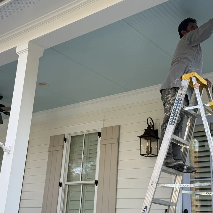 Painter on a ladder finishing a porch ceiling in pale blue on a Midlands home
